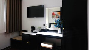 Habitaci ón de hotel con televisor de pantalla plana montado en la pared, escritorio con cafetera, florero con flores y ventana con cortinas.