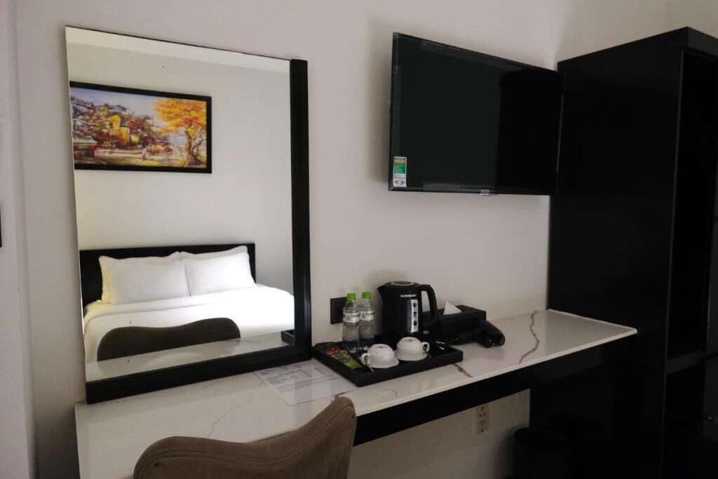 A hotel room with a bed, a TV mounted on the wall, a coffee maker, and a tray with cups and a bottle.