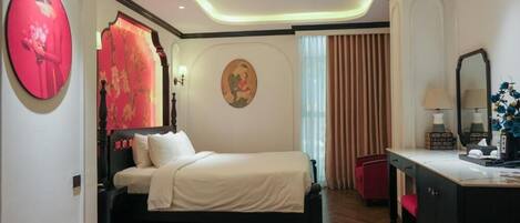 A hotel room with a bed, a desk, a chair, a mirror, and artwork on the walls.
