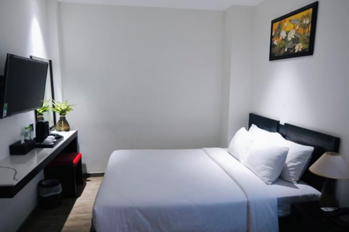 Une chambre d’hôtel avec un lit, un bureau doté d’un téléviseur à écran plat, une petite plante et un tableau au mur.