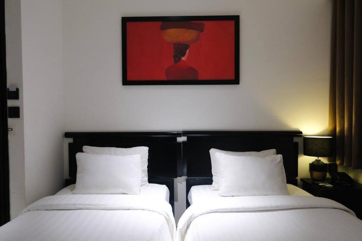 A double bed with white linens, a black headboard, and a framed artwork above.