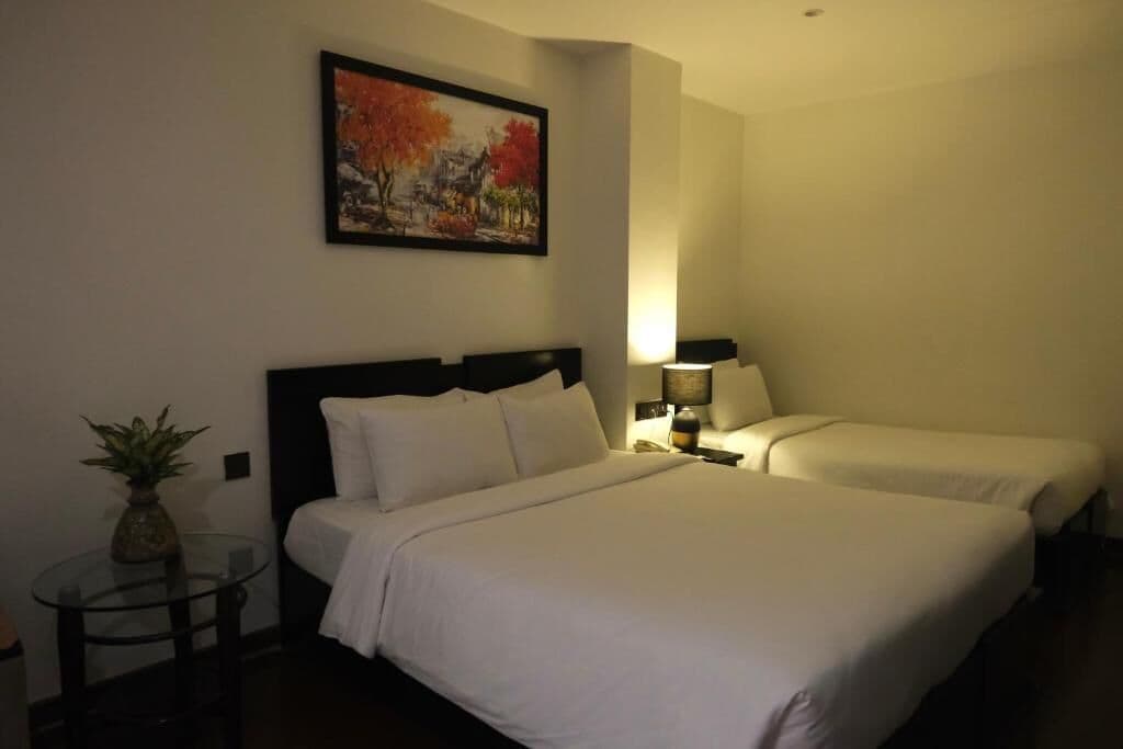 Una habitación de hotel con dos camas, una mesita con una planta y un cuadro en la pared.