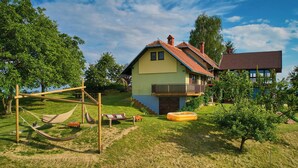 Una casa a due piani con un balcone, immersa in un prato verde con un'amaca e una piscina gonfiabile.