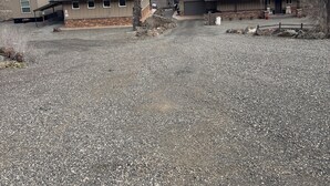 Un quartier résidentiel composé de deux maisons, chacune dotée d’un garage et d’un porche abrité. Les maisons se dressent sur un fond de collines douces et d’un ciel nuageux.