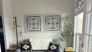 Un salon chaleureux avec un canapé gris, deux coussins décoratifs à motifs, un lampadaire noir et une plante en pot.