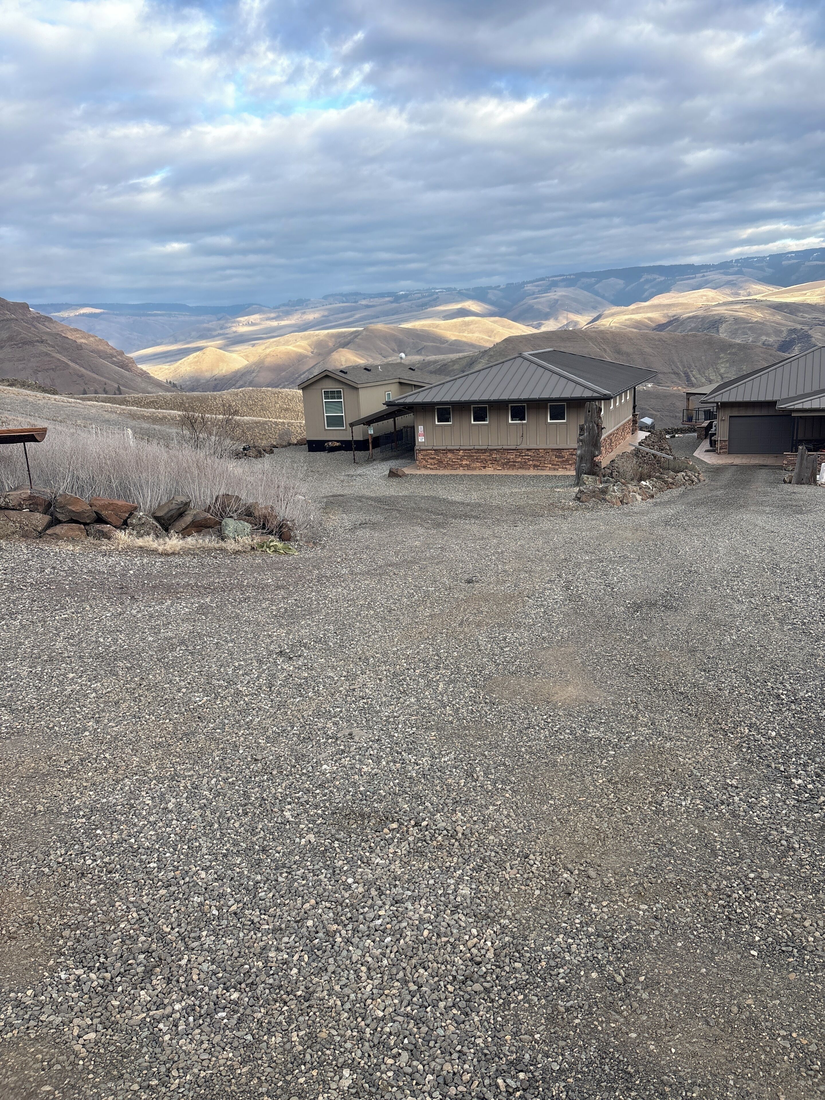 A residential area with houses, gravel driveway, and mountainous background.