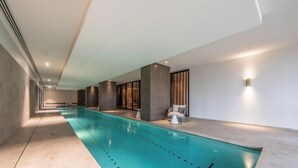 Una piscina interior moderna con diseño largo y estrecho, rodeada de paredes con asientos y luces integradas.