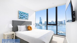 Un dormitorio moderno con una cama grande, vistas a la ciudad y un televisor montado.