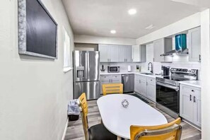 A modern kitchen with stainless steel appliances, white cabinets, and a dining table with chairs. - Stay Near Beach & Pier + Full Kitchen (Galveston)