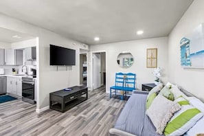 A modern living room with a sofa, a TV, a dining area with a table and chairs, and a kitchen with cabinets and appliances. - Stay Near Beach & Pier + Full Kitchen (Galveston)