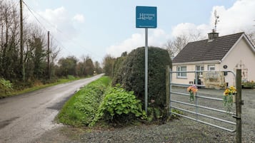 Una strada di campagna che conduce all'Harmony Lodge, una casa con vialetto sterrato e cancello in metallo decorato con fiori.