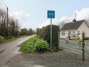 A rural road leading to Harmony Lodge, a house with a gravel driveway, and a metal gate with flowers.