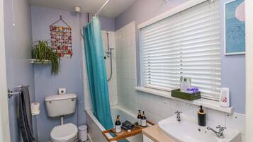 A bathroom with a toilet, sink, bathtub, shower, and a window with blinds.