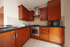 Une cuisine avec des meubles de rangement en bois, une cuisinière à gaz, un four, un four à micro-ondes et un évier.