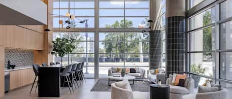 A spacious lobby with a modern design, featuring a large seating area, a kitchen, and large windows offering a view of the outdoors.