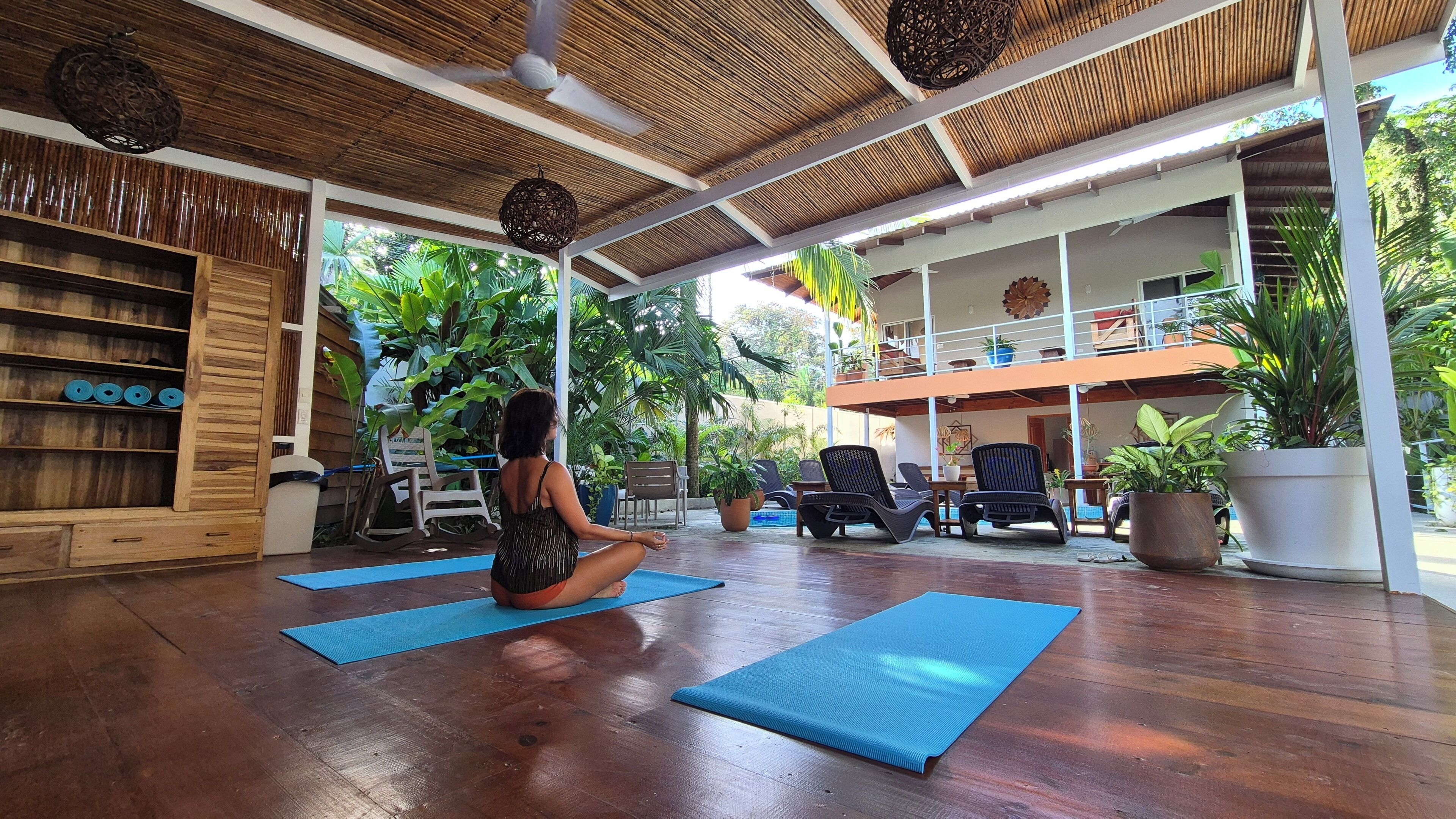 Uno studio di yoga con pavimento in legno, tappetini blu e una libreria in legno.