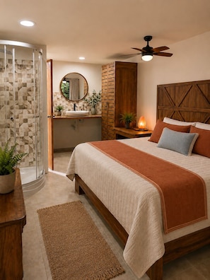 Een slaapkamer met een bed, nachtkastje, plafondventilator, houten hoofdeinde, een badkamer met douche, spiegel en een potplant.