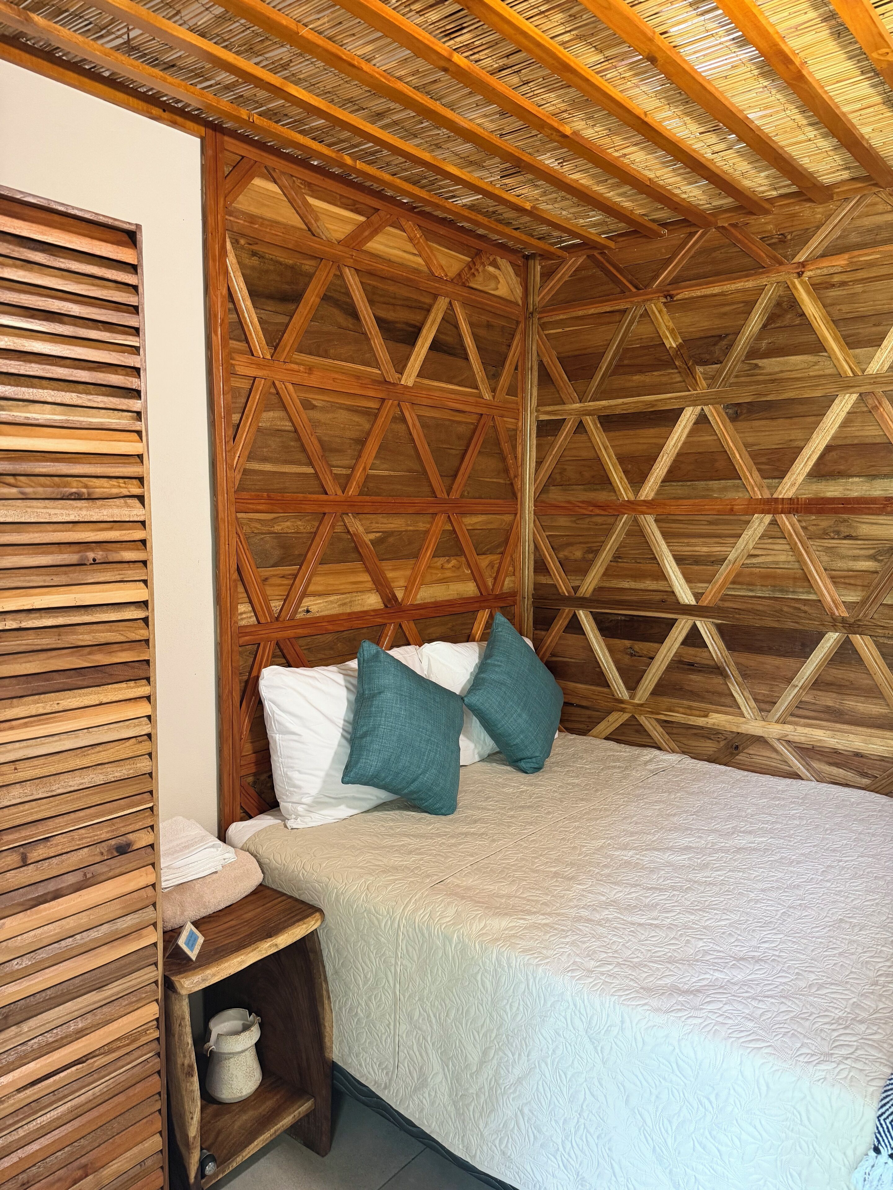 Een kamer met houten lambrisering, een bed, kussens en een klein plankje met een kan.