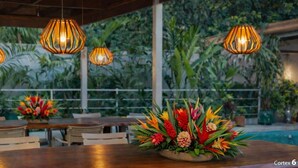 A restaurant with wooden tables and chairs, hanging pendant lights, and a floral centerpiece.