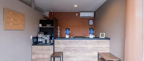 Zona de recepción con mostrador de madera, dos pequeñas mesas, un tablón de anuncios y una cámara de seguridad instalada.