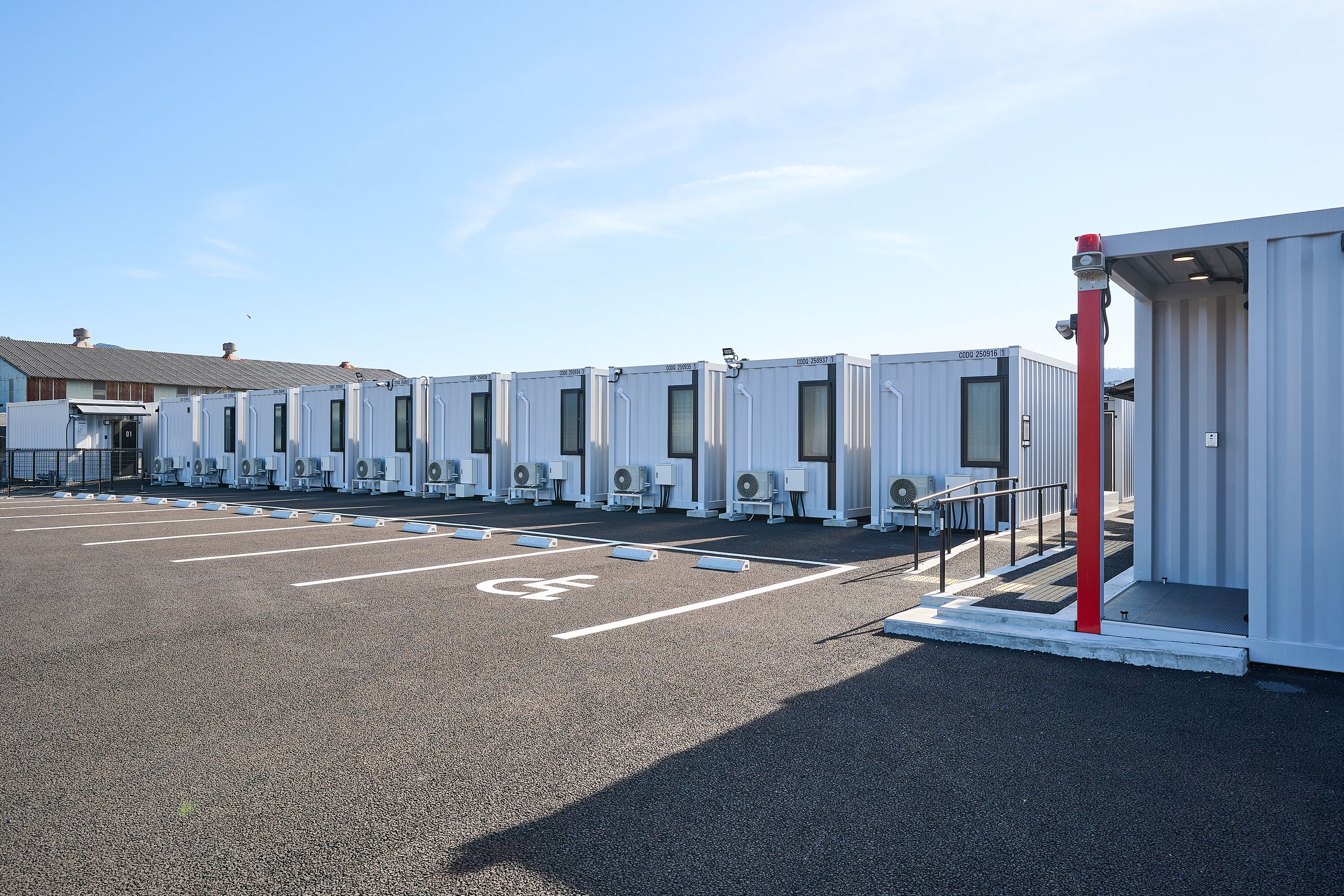 A parking lot with portable units, each with a door and windows, and a red pole near the entrance.