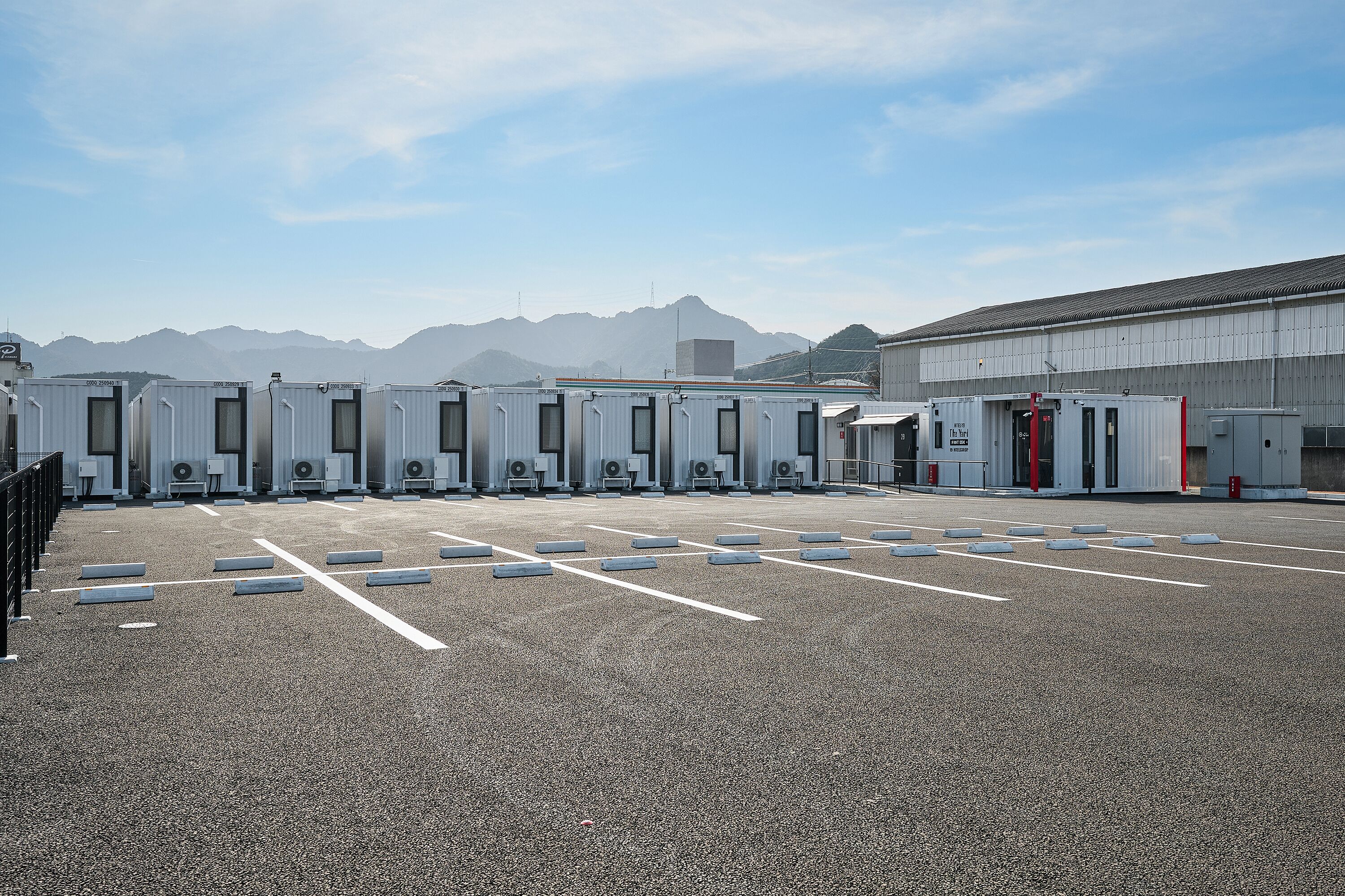 Een parkeerplaats met tijdelijke toiletten en een groot gebouw op de achtergrond.