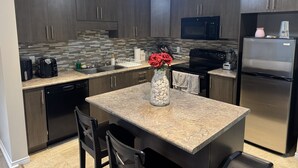 A modern kitchen with dark wood cabinets, a granite countertop, a stainless steel refrigerator, and a built-in microwave.