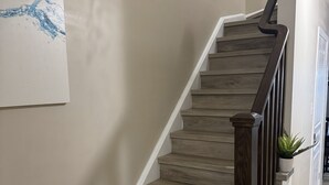 A staircase with wooden steps and a dark handrail, leading to a landing with a potted plant.