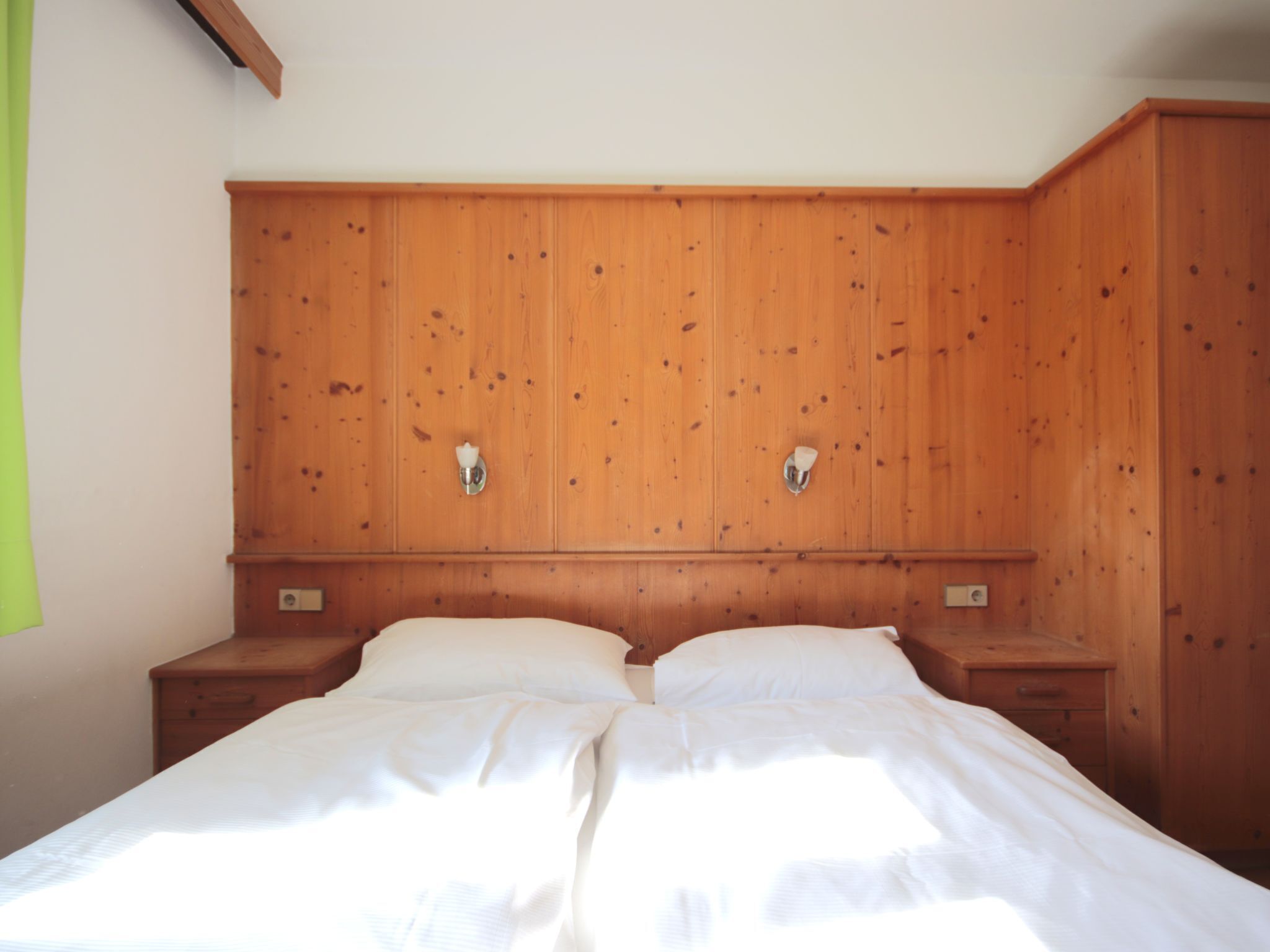Un letto matrimoniale con testiera in legno e comodini, in una stanza dalle pareti in legno e una tenda verde.