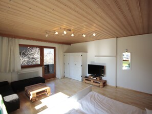 A room with a bed, a TV, a wooden coffee table, a sofa, a window with curtains, and a door. - Schlitters by Interhome (Fügen)