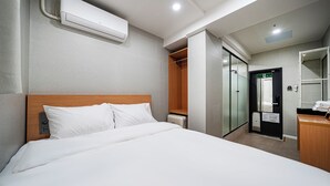 Una habitación de hotel con una cama, cabecera de madera, aire acondicionado blanco, armario y baño con espejo y toallero.