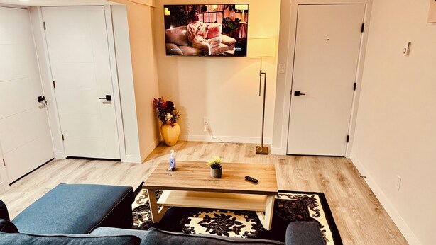 Una sala de estar moderna con sofá, una mesa de centro, televisor montado en la pared y una planta en maceta.