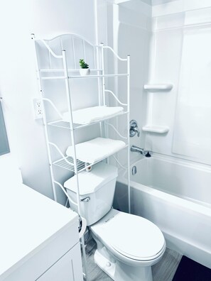 Een moderne badkamer met een wit toilet, een douche met glazen wand en een witte metalen plank met een kleine plant.