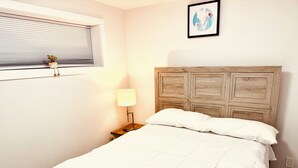 Una cama bien hecha con cabecera de madera, una lámpara de noche y una ventana con persianas.