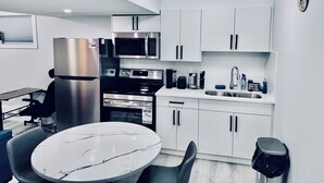 Una cocina moderna con armarios blancos, electrodomésticos de acero inoxidable, encimera de mármol y una zona de comedor con mesa y sillas.