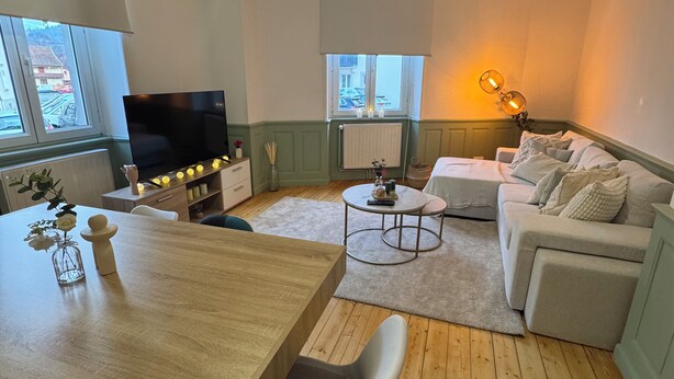 Ein modernes Wohnzimmer mit einem Holzesstisch, einer Couch und einem Fernseher.