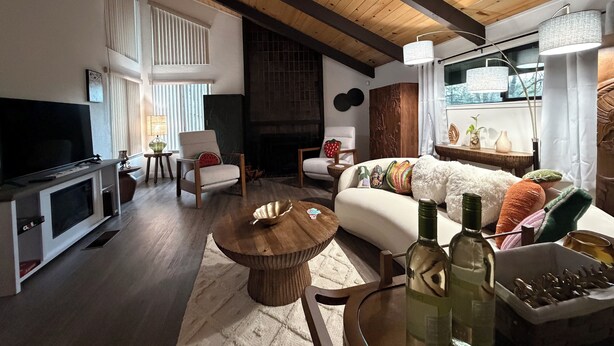 A living room with a wooden ceiling, a television, a sofa with colorful pillows, and a fireplace.