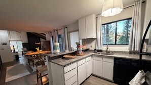 A modern kitchen with white cabinets, a granite countertop, and a large window with a view of trees.