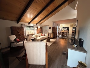 A spacious living room with a high ceiling, wooden beams, a sofa set, a dining area, and a kitchen in the background. - 30 Mins to Yosemite: 2BR Retreat with Lake & Golf (Groveland)
