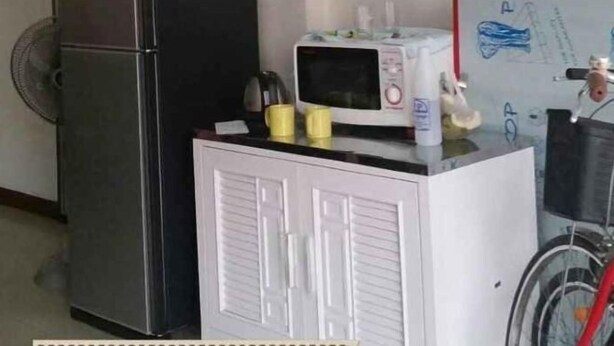 Een keuken met een koelkast, magnetron en een witte kast, met een fiets die er buiten staat geparkeerd.