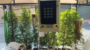 Een numeriek keypad beveiligingsapparaat bevestigd aan een paal, omringd door potplanten en tuinmeubilair.