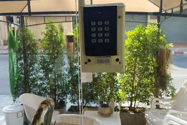 Un dispositif de sécurité à clavier fixé sur un poteau, entouré de plantes en pot et de mobilier d’extérieur.