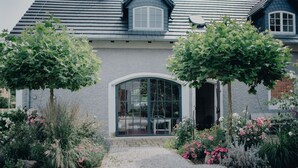 A house with a gravel driveway, a large arched entrance, and a garden with various plants and flowers. - Quiet apartment above the Bobertal valley in the foothills of the Giant Mountains (Tarczyn)