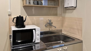 Una kitchenette compacta con microondas, tetera, pileta y un estante superior con tazas y vasos.