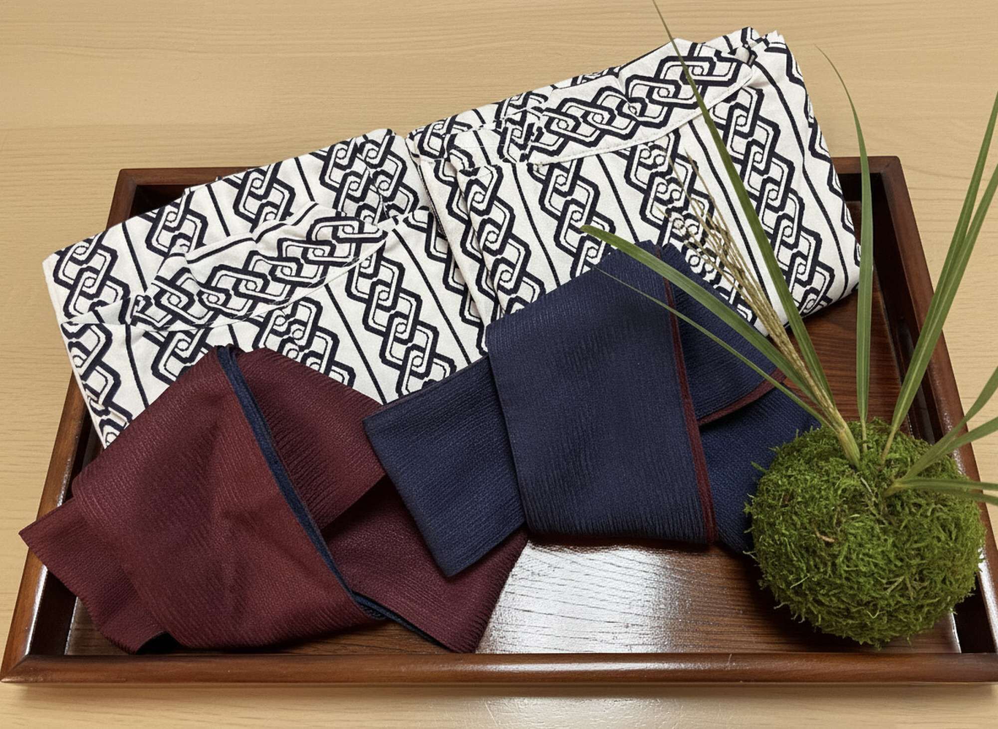 Een houten dienblad met een gestreept laken, een donkerblauwe doek en een bordeauxrode doek.