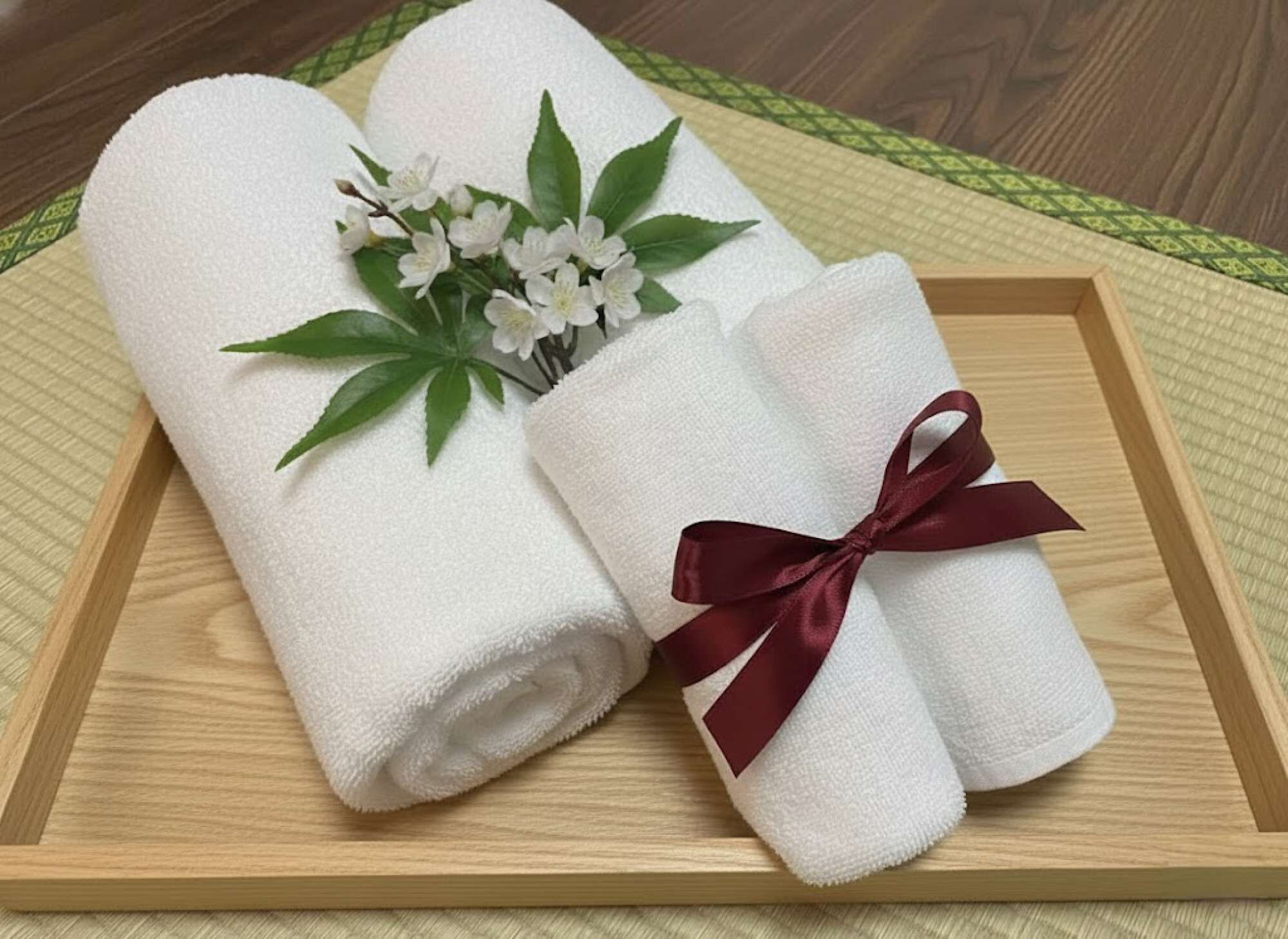 Toallas blancas dobladas con cuidado, una adornada con un lazo decorativo, sobre una bandeja de madera.