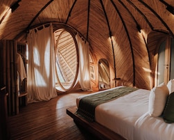 Una habitación circular y acogedora con techo de madera, una cama y un ventanal con cortinas.