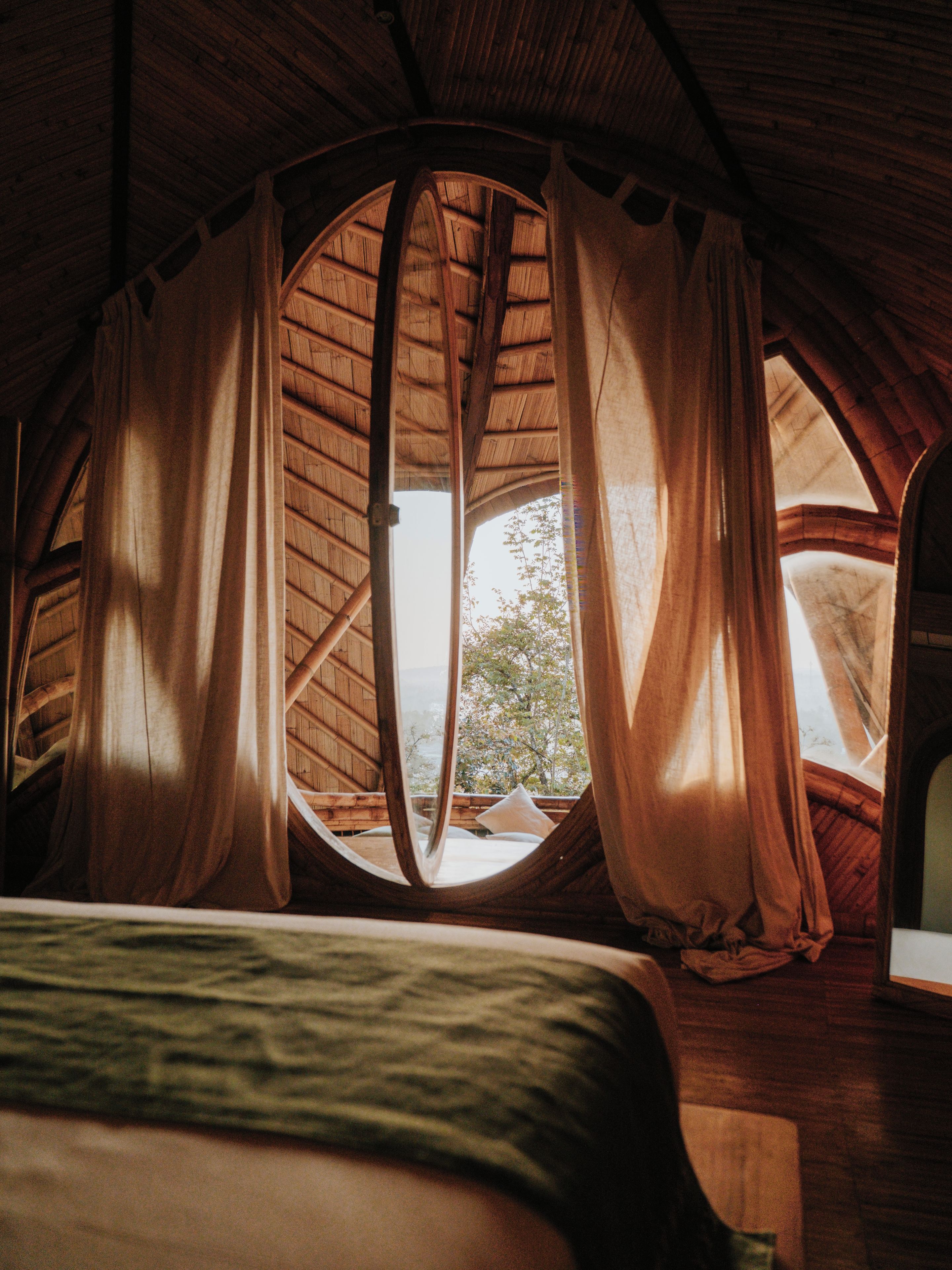 A room with a bed, curtains, and a view through a window.