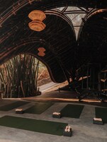 Un espacio interior con estructura de techo curva, colchonetas de ejercicio y bloques de madera.