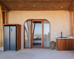 A modern kitchen with a built-in refrigerator, a wooden cabinet, and a view through a glass door. - Cocoon Reserve (Kuta)